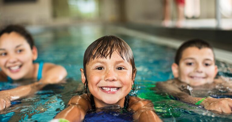 Girls and boy swimming in pool with kickboards